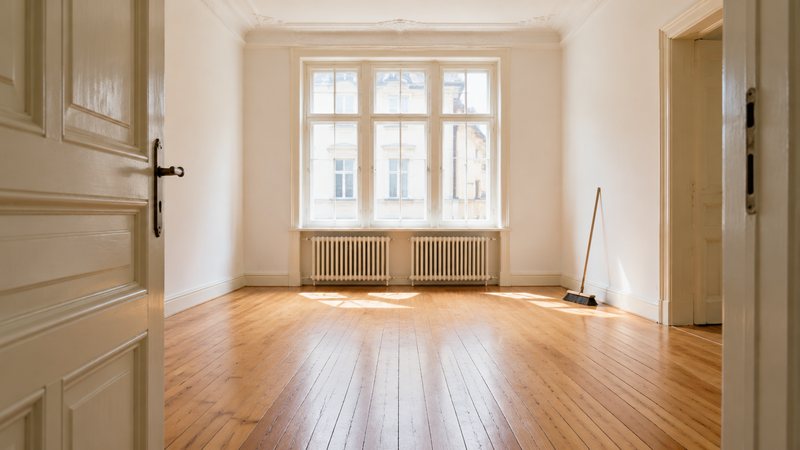 Besenrein nach der Entrümpelung: leergeräumtes Altbauzimmer mit Dielenboden, Besen an der Wand, Licht fällt durchs Fenster